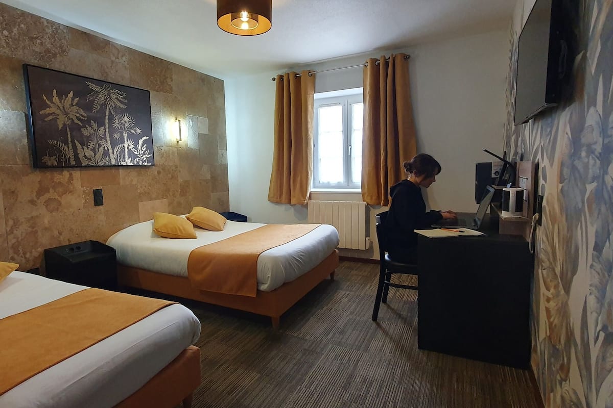A hotel room with two beds, a desk, a TV, and a window with curtains.