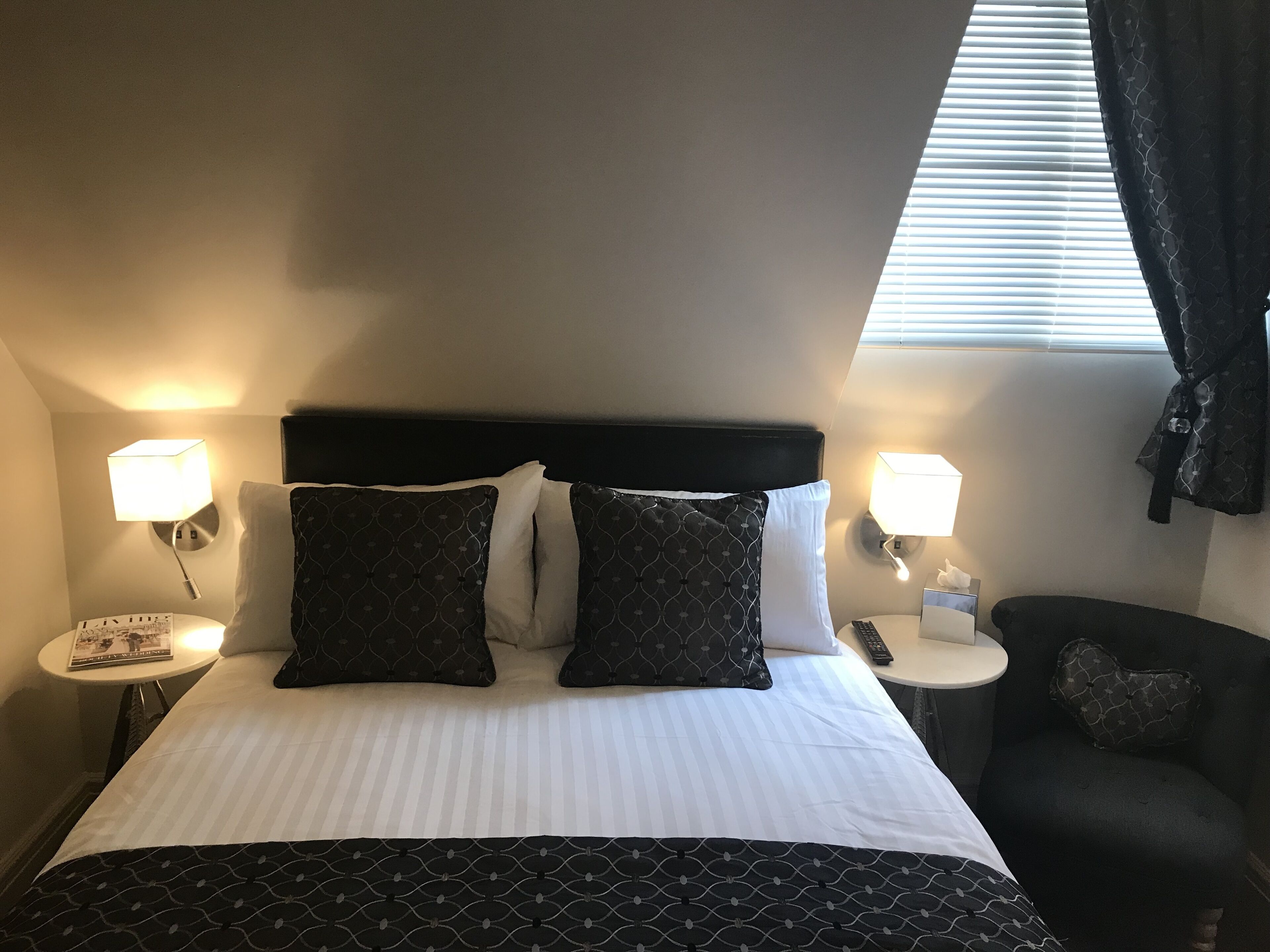 A hotel room with a bed, two bedside lamps, a nightstand, a chair, and a window with blinds.
