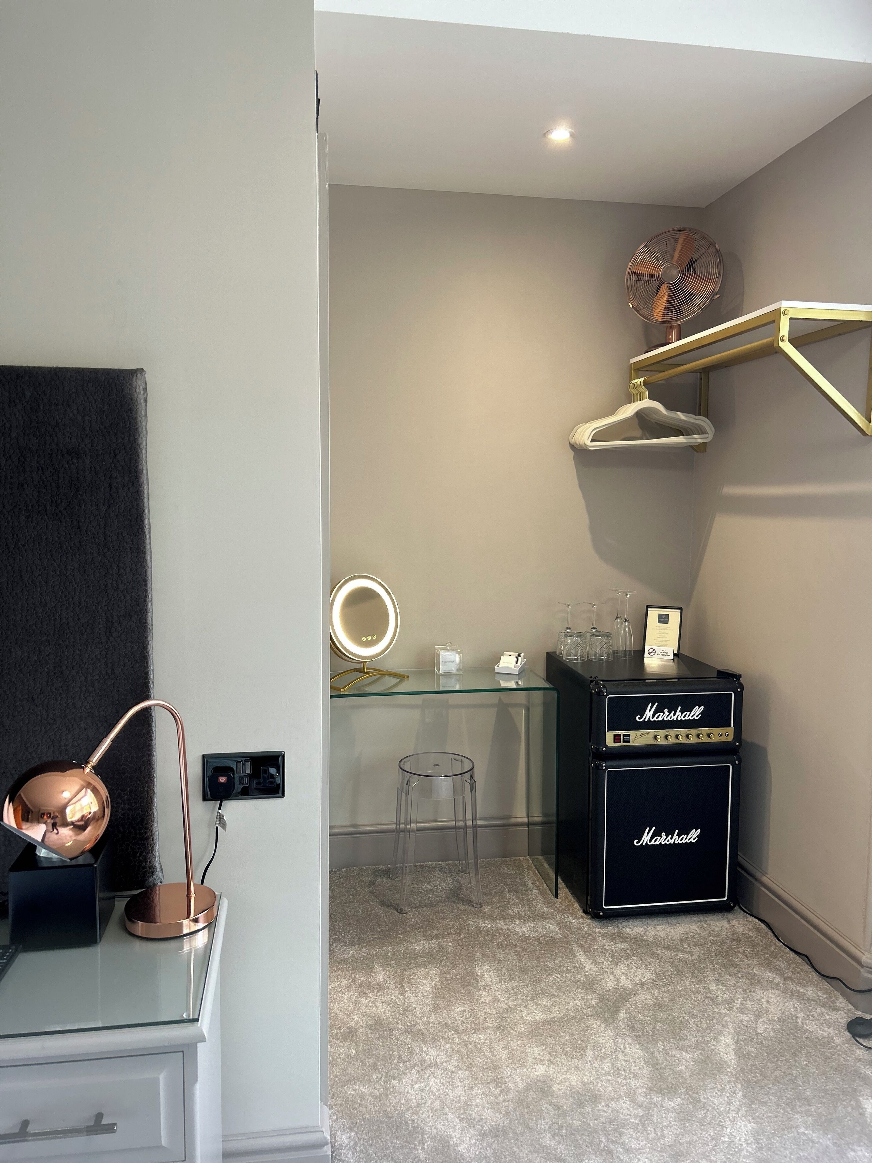 Une salle de bain moderne avec un meuble-lavabo en verre, un miroir rond, un porte-serviettes et une paire d’amplificateurs Marshall.