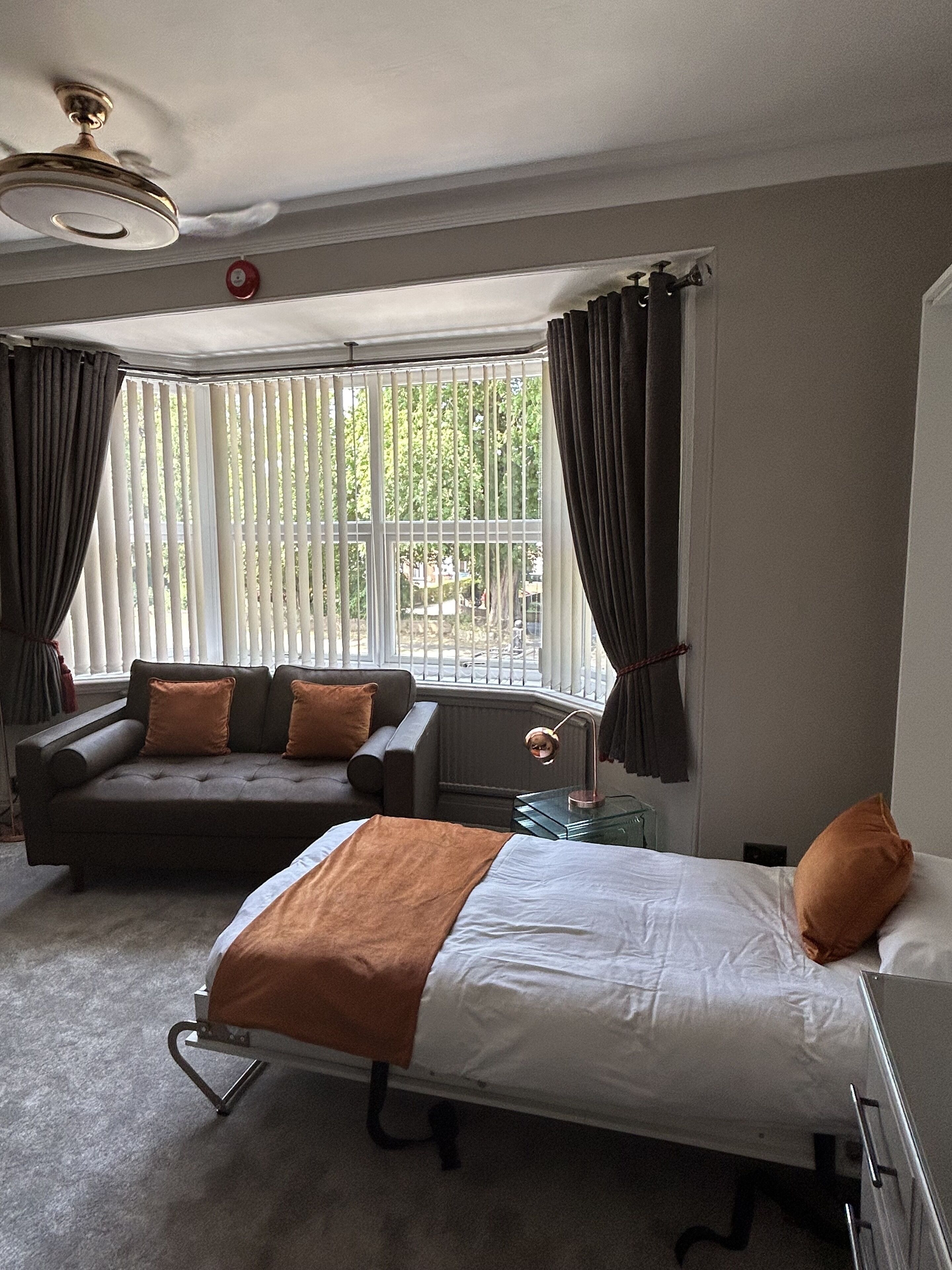 Habitación de hotel con cama, sofá, una mesita y una ventana con persianas.