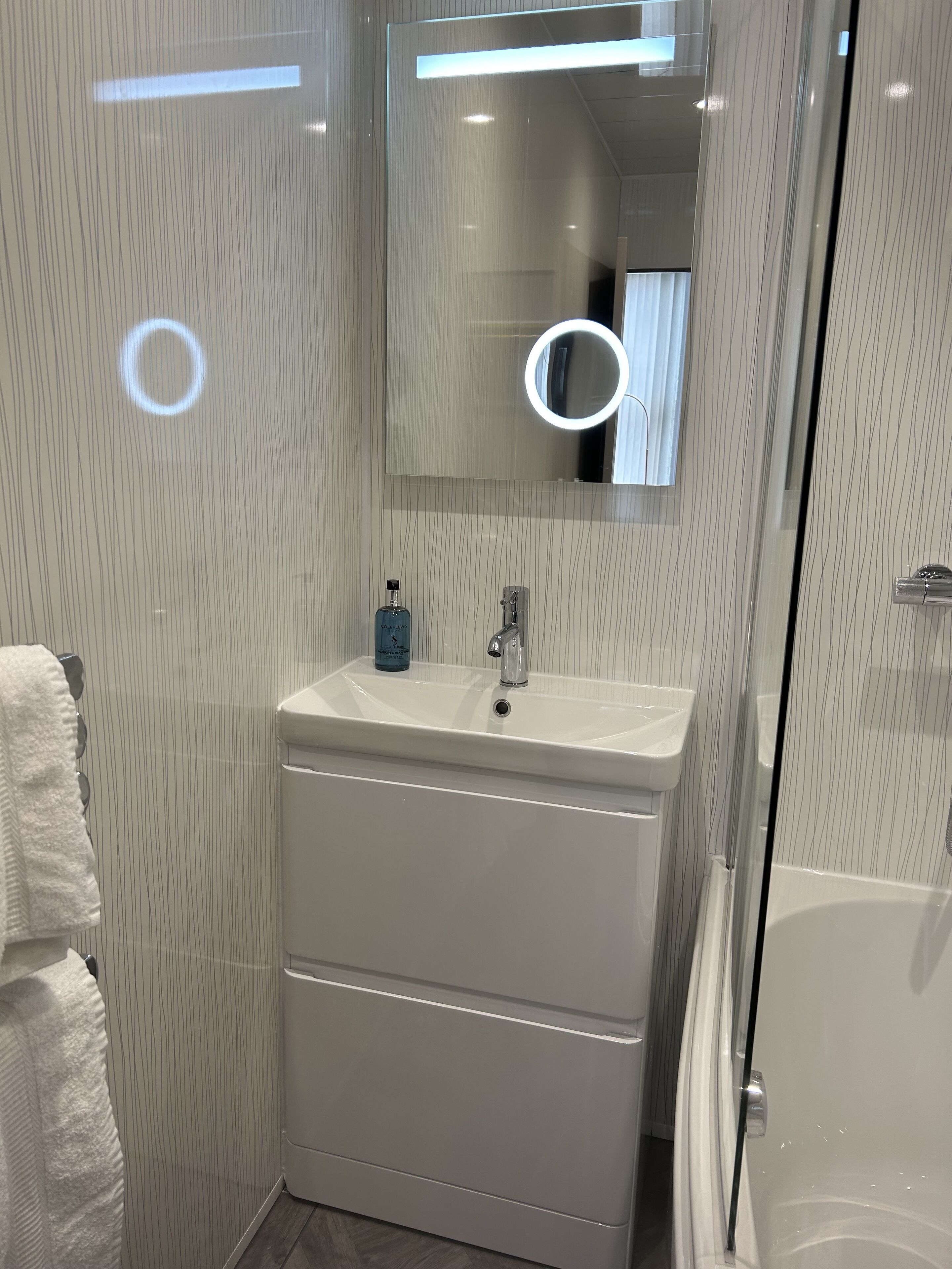 Une salle de bain moderne avec un lavabo blanc, un miroir et une cabine de douche en verre.