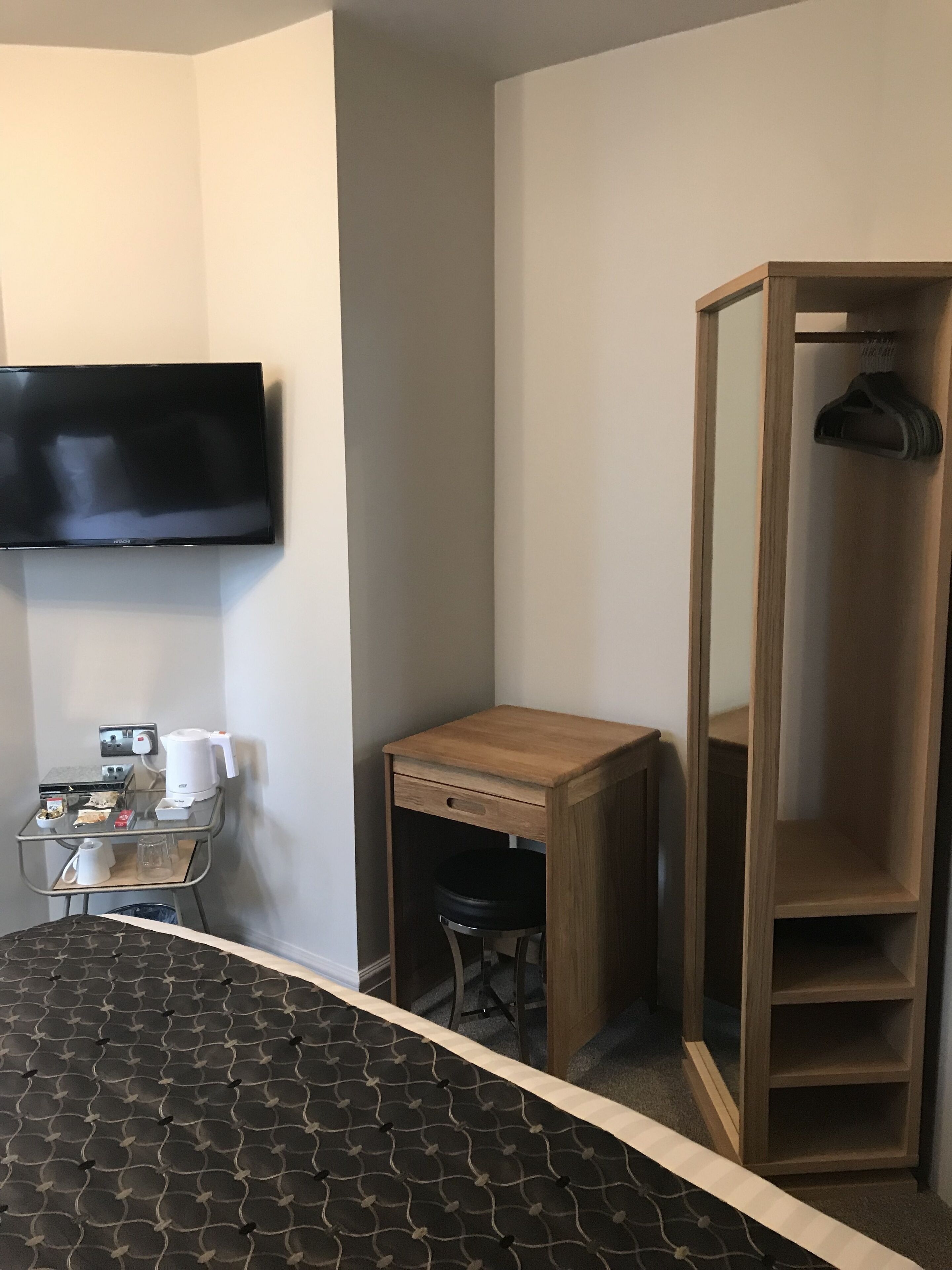 Habitación de hotel con cama, televisor montado en la pared, escritorio de madera, silla y armario.