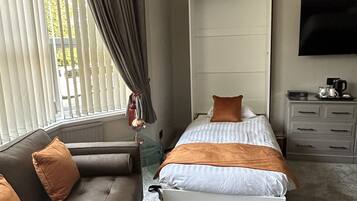 Un dormitorio con cama, sofá, televisor y ventana con cortinas.