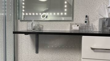 A bathroom with a vanity, a mirror with lights, a stool, and a hand dryer.