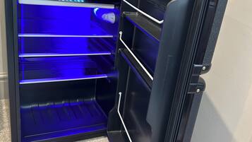 An open refrigerator with a blue light inside, a 'No Smoking' sign, and a framed certificate on top.
