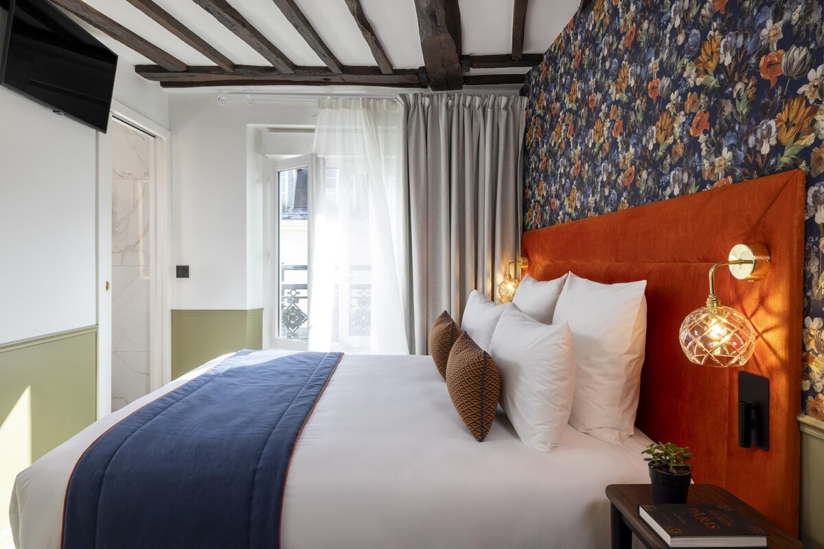 Ein Hotelzimmer mit einem Bett, einem Nachttisch, einer Topfpflanze und einer Wand mit Blumenmuster-Tapete.