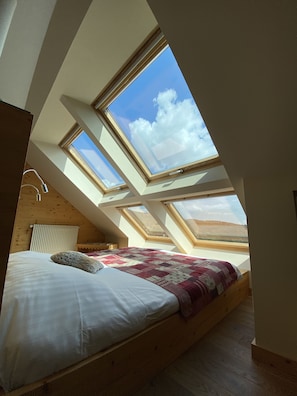 A bedroom with a sloped ceiling and skylights, a bed with a quilt, and a radiator. - Le Clos des Sources Hôtel*** & Spa (Thannenkirch)