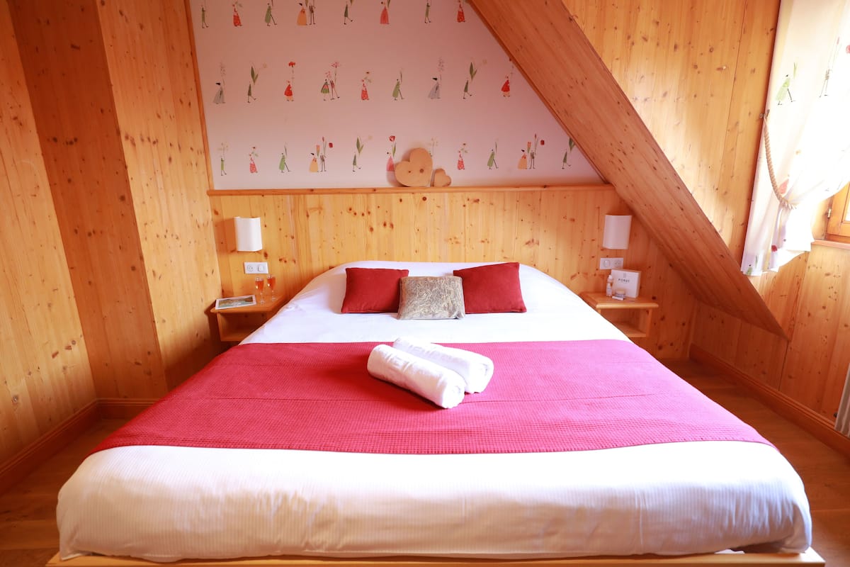 A bedroom with a large bed, wooden walls, and a sloped ceiling.