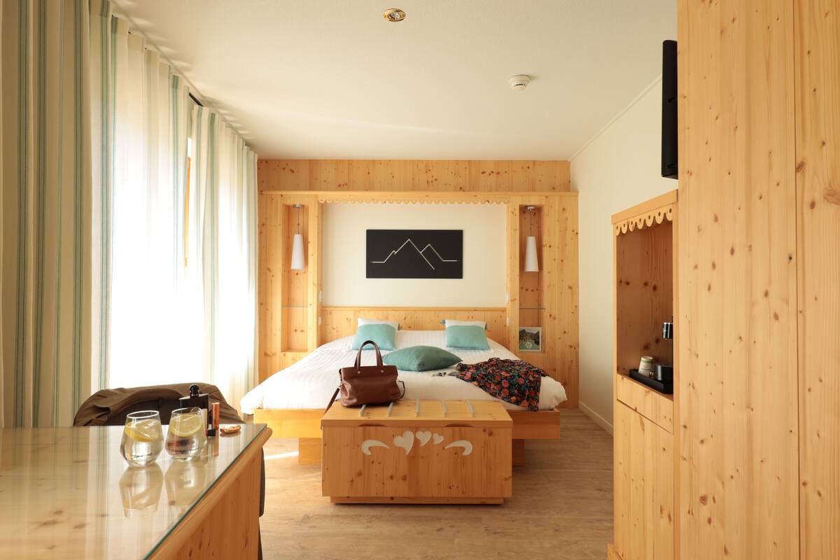 A modern hotel room with a wooden bed, a flat-screen TV, a wooden nightstand, and a large window with curtains.