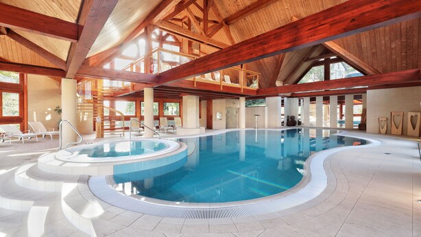 Una piscina interior con techo de madera y un espacio luminoso con sillones de descanso.