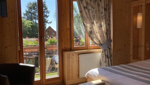 Habitación de cabaña de madera con una cama, una silla y vistas a un jardín a través de amplios ventanales.