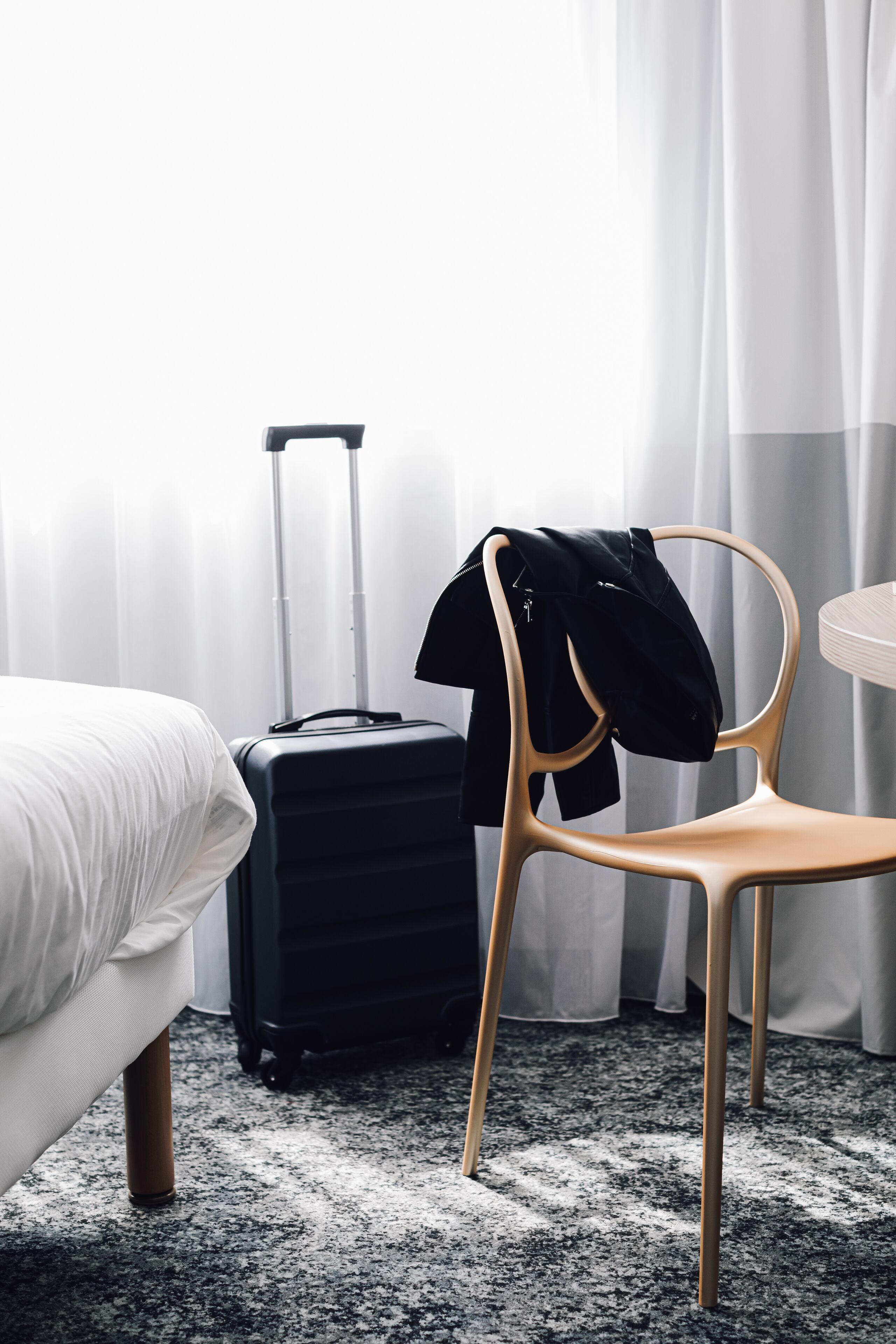 A hotel room with a bed, a chair, a suitcase, and a table.
