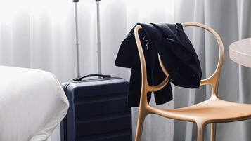A hotel room with a bed, a black suitcase, a wooden chair, and a table.