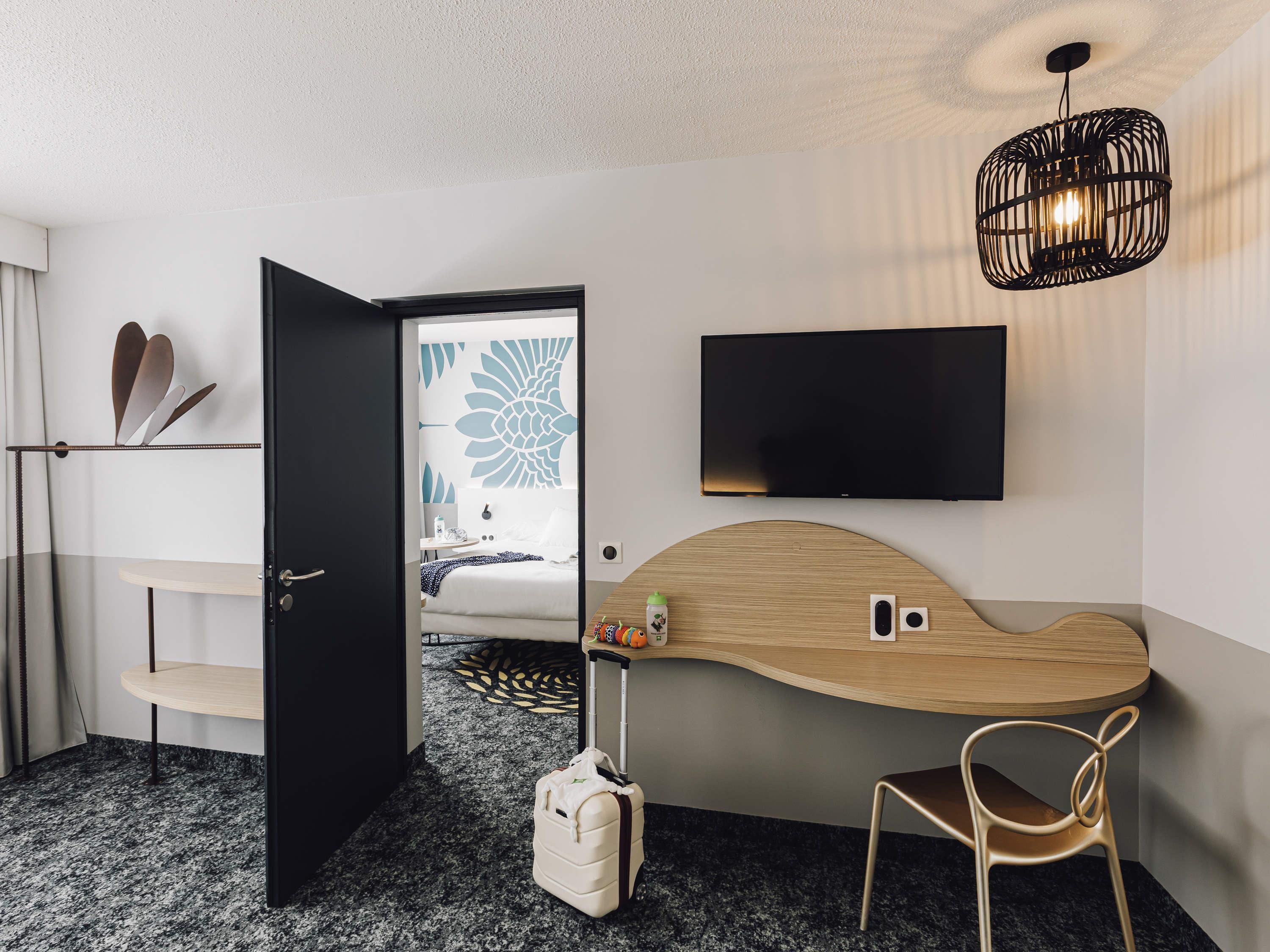 A hotel room with a bed, a desk, a chair, a television, and a luggage bag.