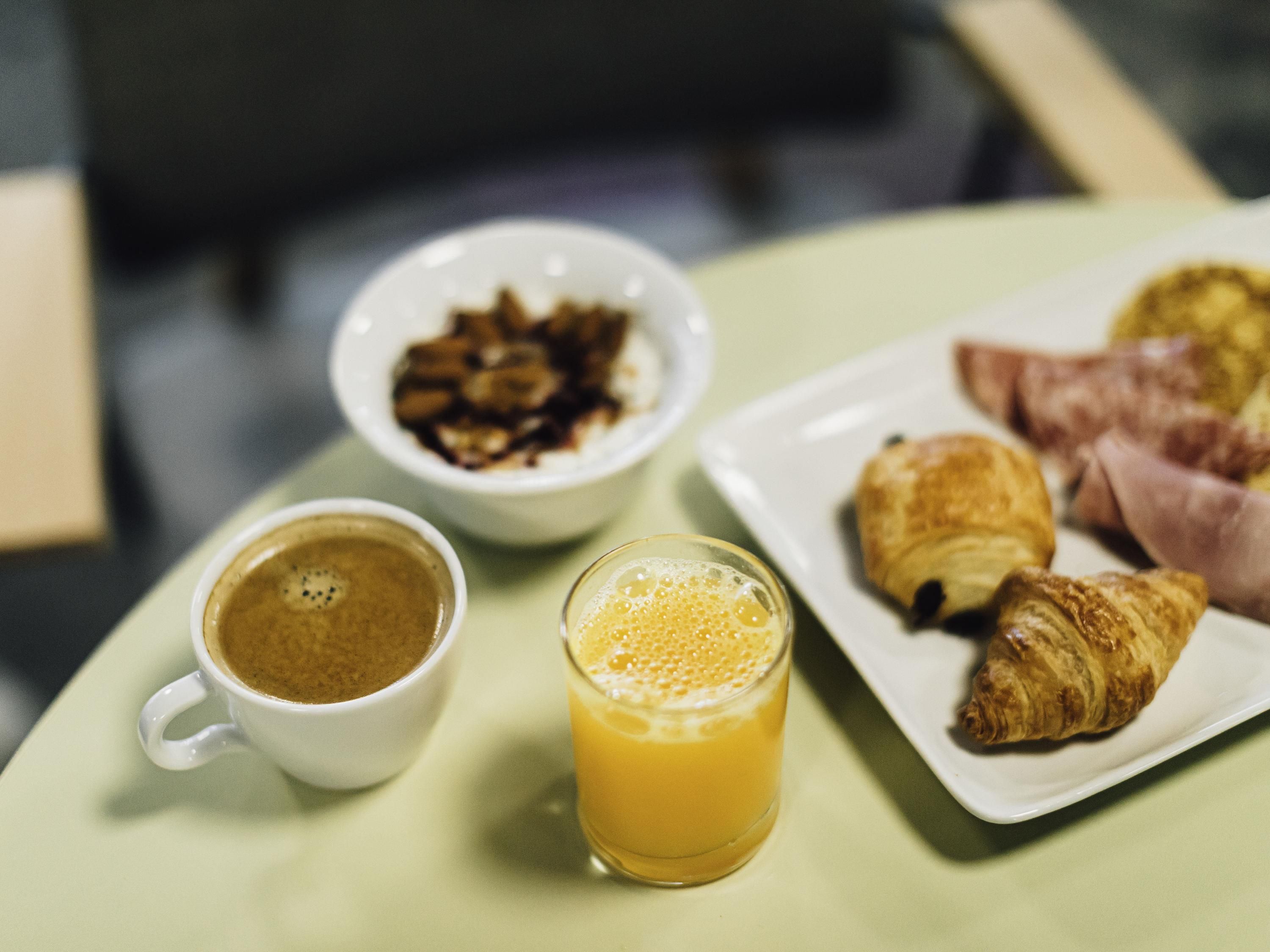 A breakfast setting with a cup of coffee, a glass of orange juice, a plate of croissants, and a bowl of cereal.