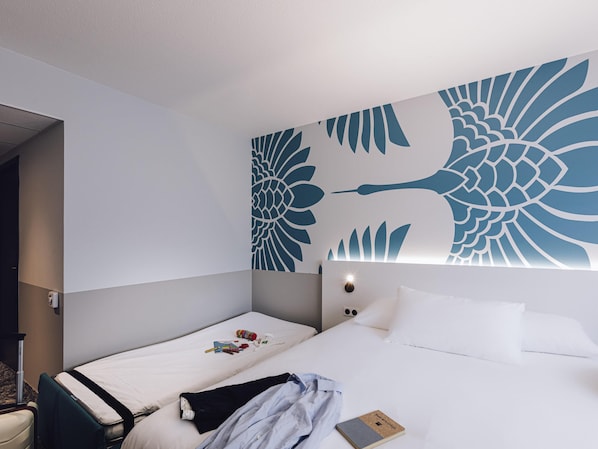 A hotel room with two beds, a large wall mural, a bedside table, and a nightstand.