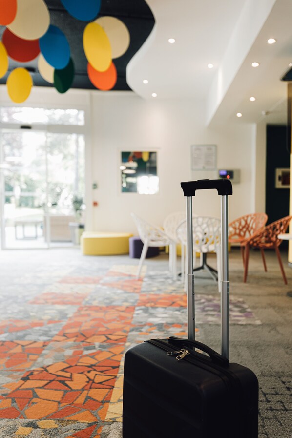 A black suitcase with wheels in a hotel lobby with colorful ceiling decorations, a patterned carpet, and a seating area with chairs.