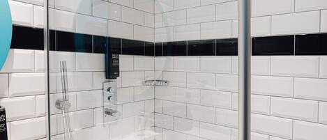Un baño moderno con azulejos blancos tipo metro, cabina de ducha de vidrio y lavamanos blanco con espejo.