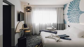A hotel room with a bed, a desk, a chair, a television, a suitcase, and a window with curtains.
