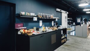 A well-lit reception area with a counter displaying various food items and beverages, a coffee machine, and a shelf with packaged goods. - ibis Styles Nancy Laxou (Laxou)