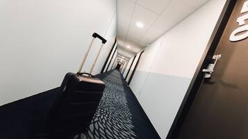 A hotel corridor with a patterned carpet, a suitcase, and a door with a number.