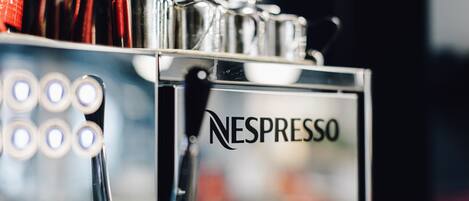 Primer plano de una máquina de café Nespresso, con varias cápsulas de café y un depósito de agua.
