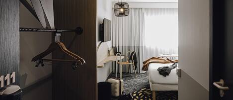 A hotel room with a bed, a desk, a chair, a wardrobe, and a bathroom.
