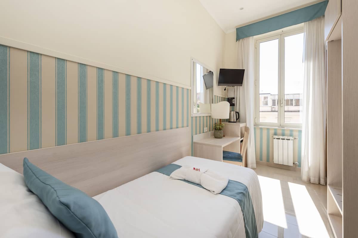 Une chambre d’hôtel avec deux lits, un bureau doté d’un téléviseur à écran plat, une fenêtre avec des rideaux et une vue sur l’extérieur.