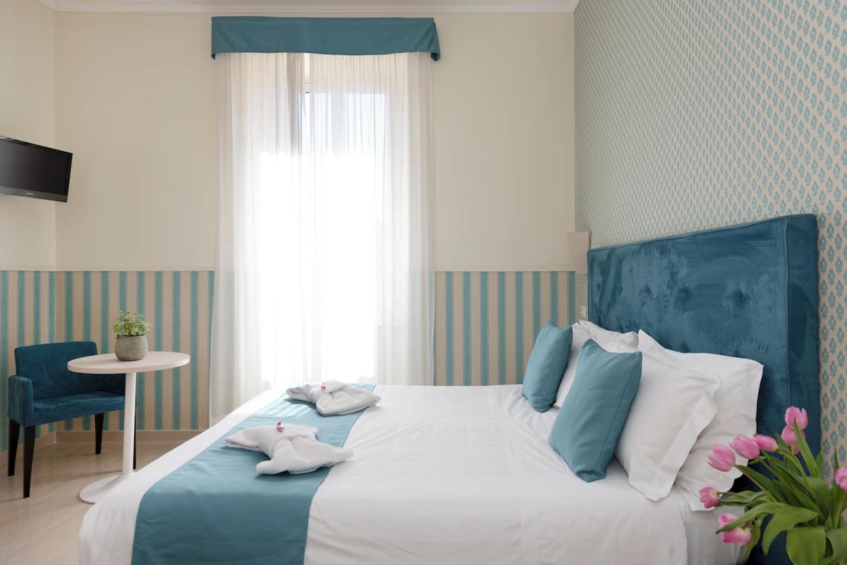 Une chambre d’hôtel avec un lit, une petite table, une chaise et un téléviseur fixé au mur.