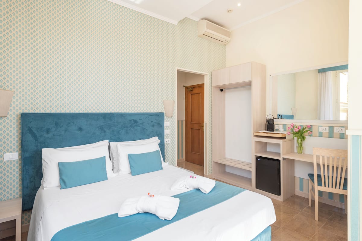 Une chambre d’hôtel comprenant un lit, un bureau, une chaise, une armoire et une petite kitchenette.