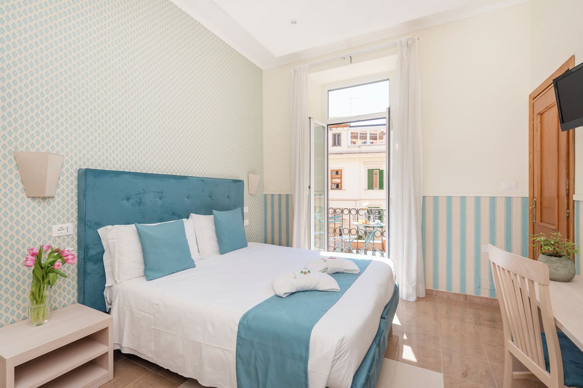 Une chambre d’hôtel comprenant un lit, une table de chevet, une chaise, une télévision et un balcon avec vue sur les immebles.