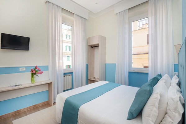 A hotel room with a bed, a TV mounted on the wall, a window with curtains, a bedside table with a vase of flowers, and a view of buildings outside. - Parker (Rome)