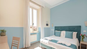 A bedroom with a bed, a chair, a window, and a small table.