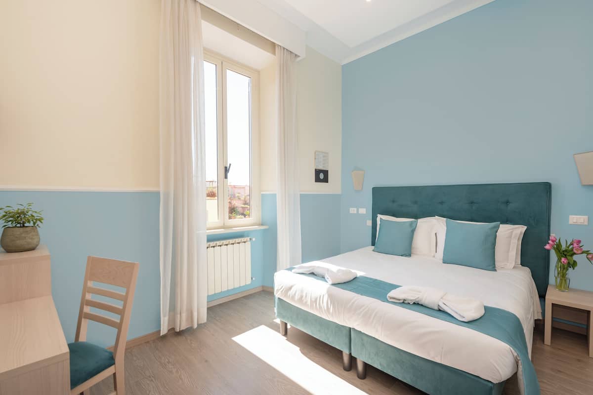 Une chambre à coucher avec un lit, une chaise, une fenêtre avec des rideaux et un radiateur.