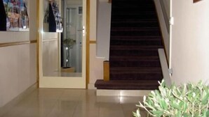 A staircase with a dark carpet and wooden handrails, leading to a room with a glass door and a small plant on the floor. - Hôtel Pacific (Calais)