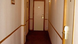 A narrow hallway with a carpeted floor, wooden trim, and a door at the end. - Hôtel Pacific (Calais)