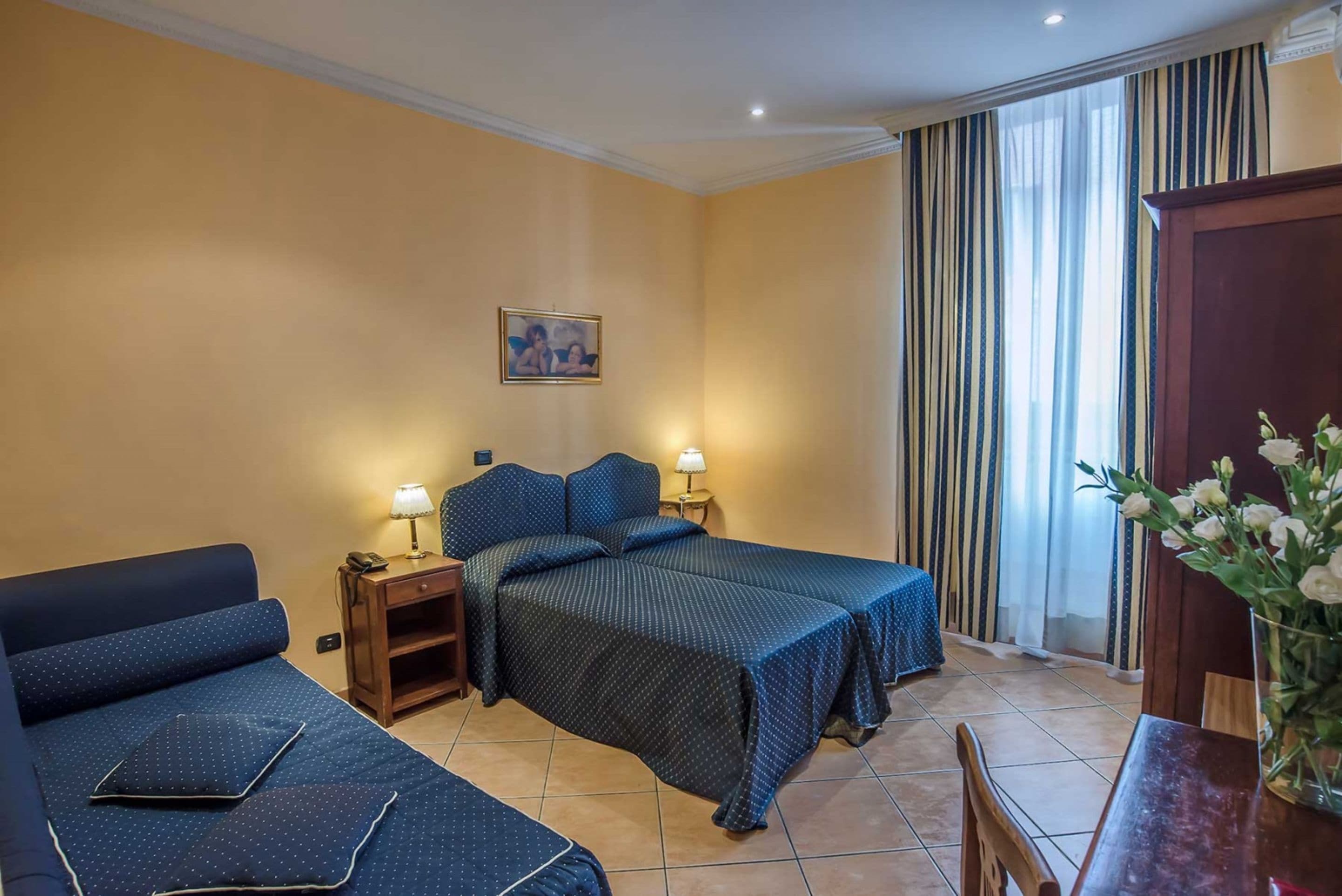 A hotel room with two beds, a sofa, a small table, and a window with curtains.