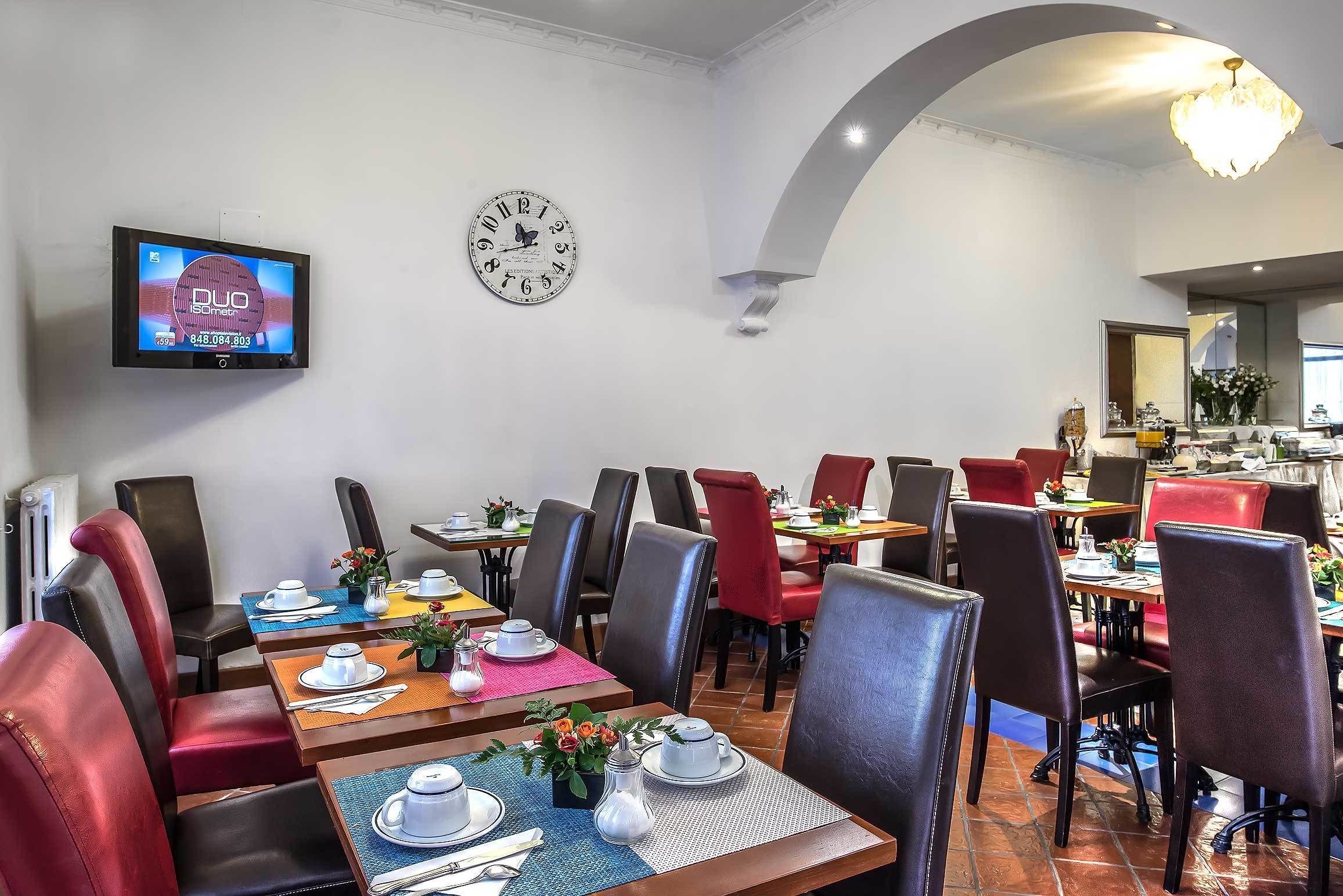 A dining area with tables set for service, a wall clock, and a television displaying 'Duo 15mtr'.