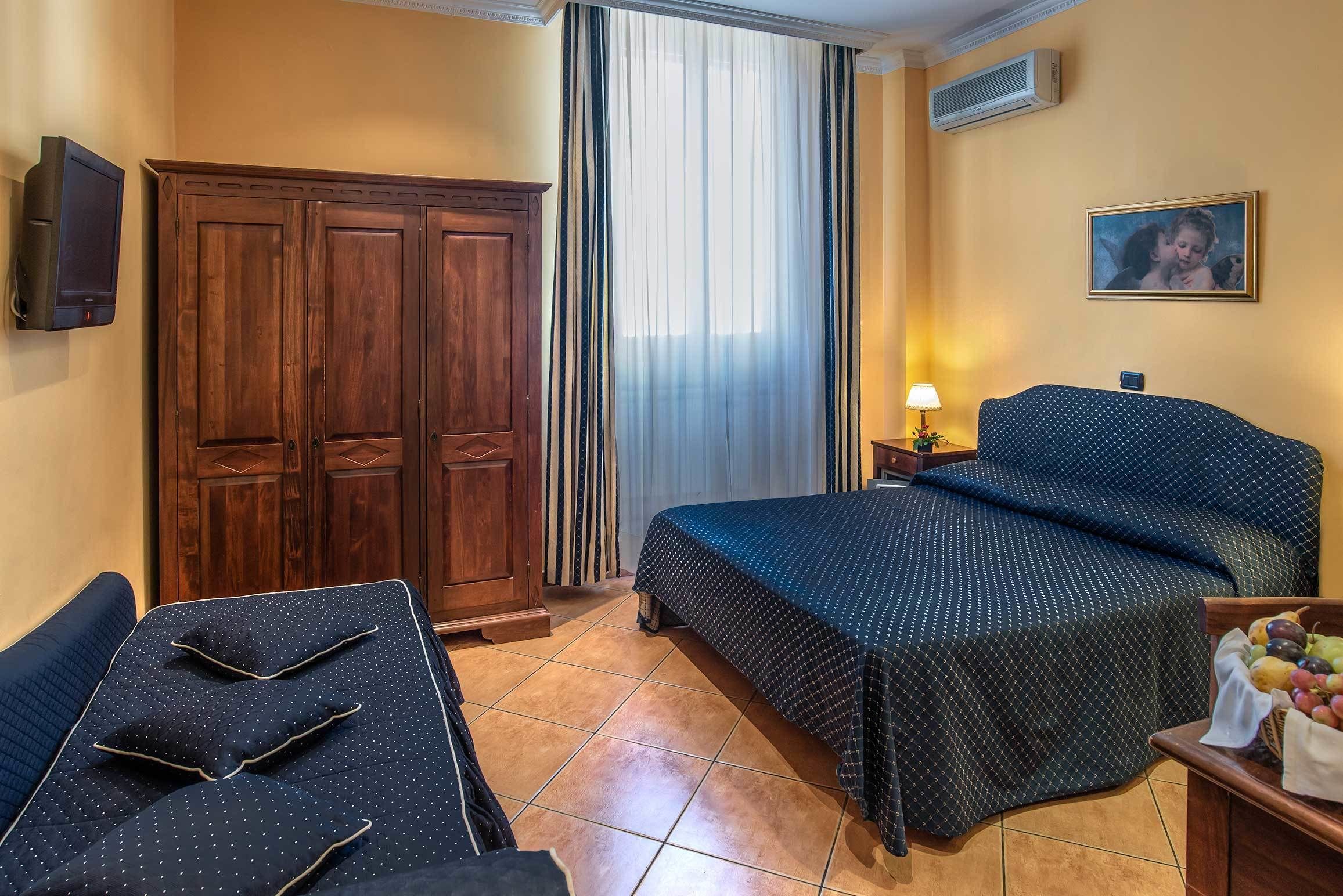 A hotel room with a bed, a desk, a wardrobe, a TV, a lamp, and a framed picture on the wall.