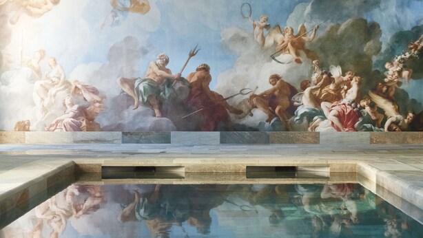 Een zwembad met een spiegelend oppervlak en een muurschildering van mythologische figuren.