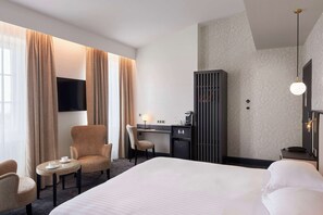 Habitación de hotel con una cama grande, un escritorio con una silla, una mesita con tazas y un televisor montado en la pared.
