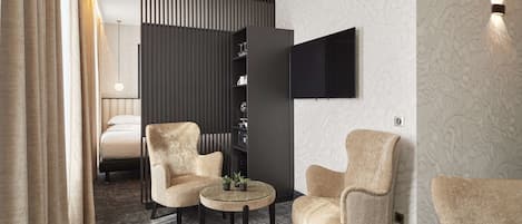 A modern hotel room with a bed, two armchairs, a small round table, a bookshelf, and a flat-screen TV mounted on the wall.