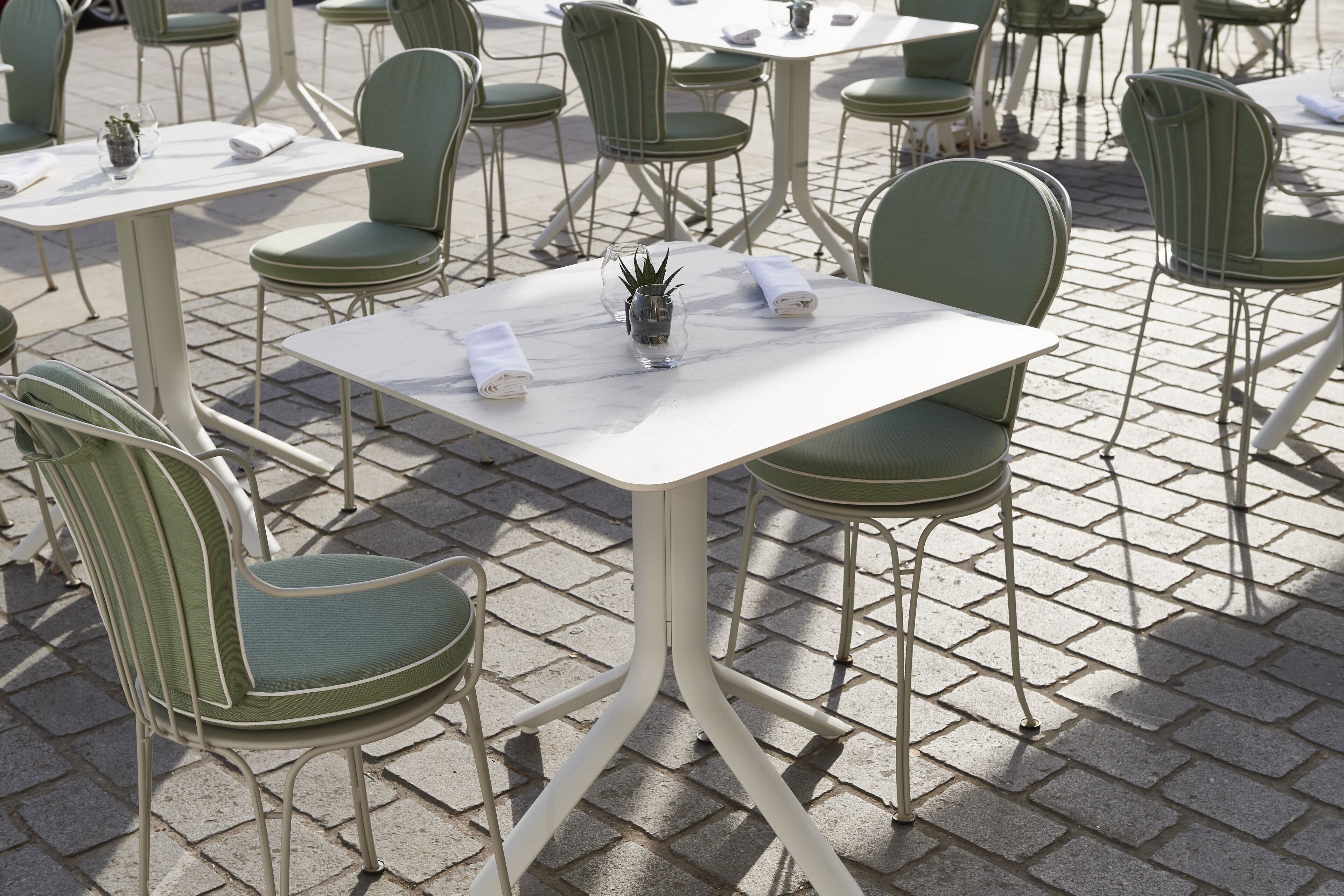 Un espace patio aménagé avec des chaises à l’assise verte et des tables à plateaux en marbre blanc, disposées sur une surface pavée.