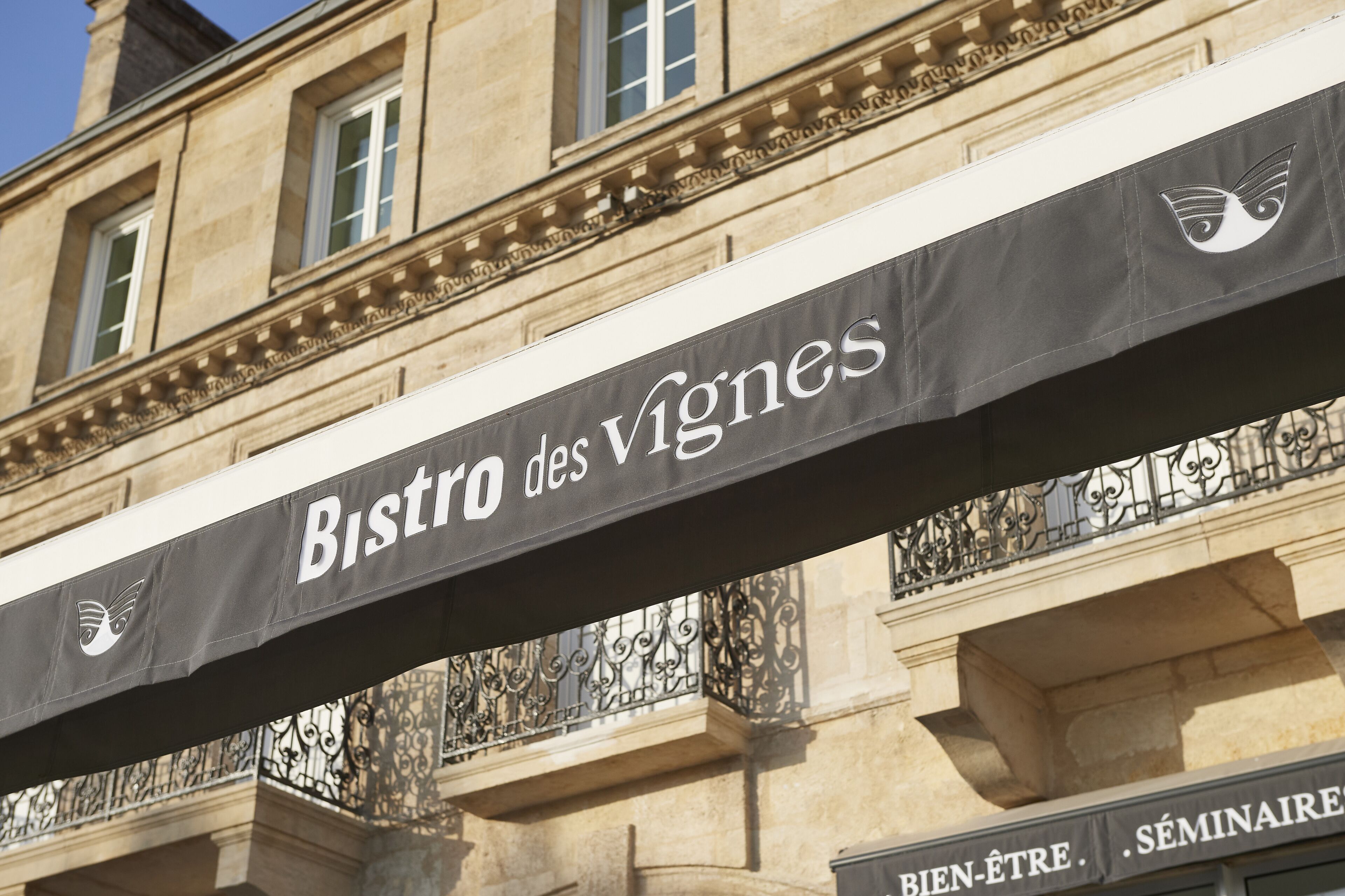 Une enseigne pour le Bistro des Vignes, avec la façade d’un bâtiment classique en arrière-plan.