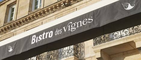 Une enseigne pour le Bistro des Vignes, avec la façade d’un bâtiment classique en arrière-plan.