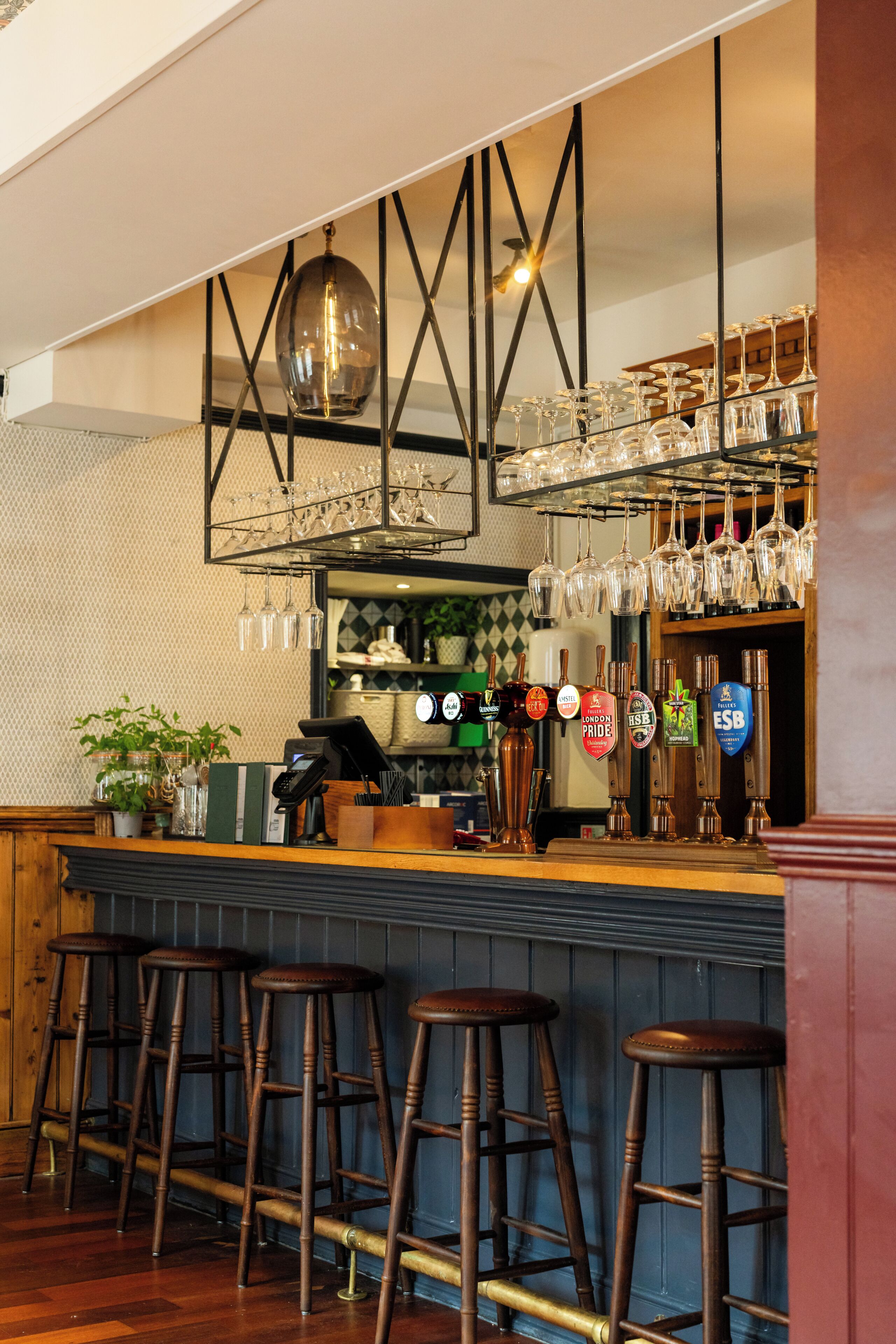 A bar area with stools, a counter, and a selection of glasses and bottles.