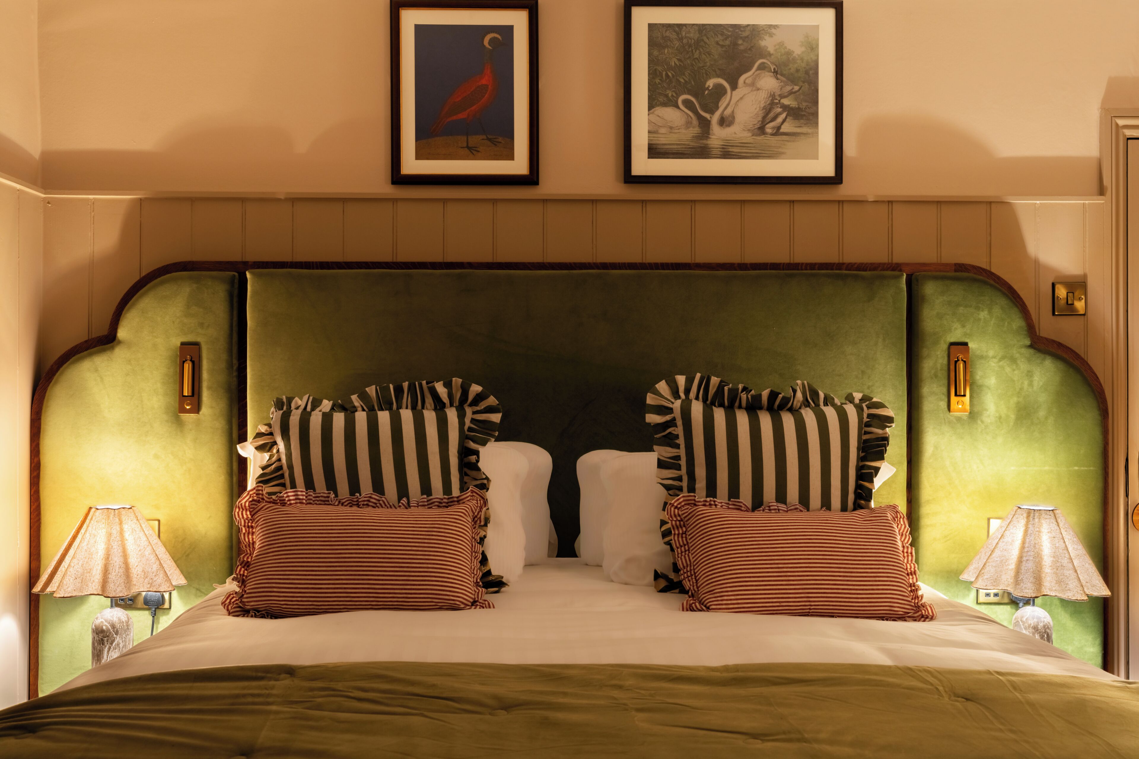 Un lit avec des coussins à rayures, une tête de lit recouverte d’un tissu vert et deux tableaux encadrés accrochés au mur.