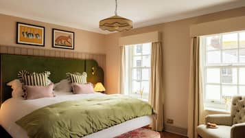 A neatly made bed with a green headboard, a striped armchair, and a window with curtains.
