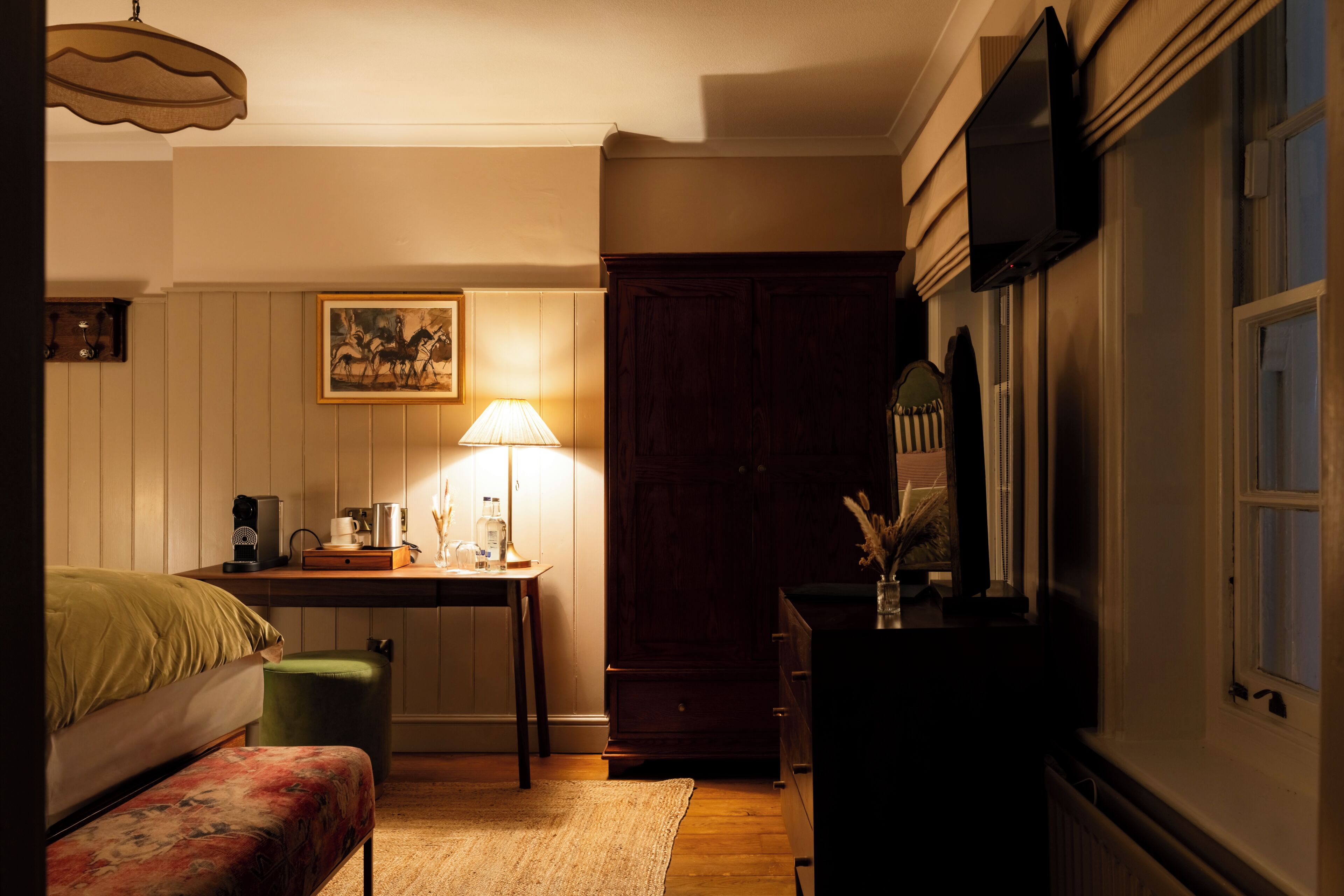 Une chambre à coucher avec un lit, un bureau avec une lampe, une commode et un téléviseur fixé au mur.