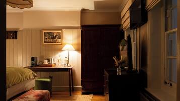 Quarto com uma cama, escrivaninha com luminária, cômoda e televisão na parede.